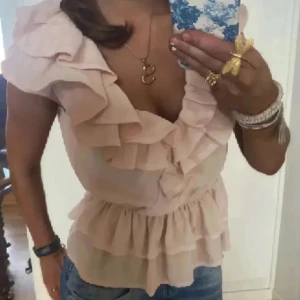 Rosa volangblus - Säljer en söt rosa blus med volanger och djup v-ringning. Blusen hade gått sönder i v-ringen men jag har sytt och syns inte (skriv privat för bild). Den har även några fläckar (syns knappt)!!