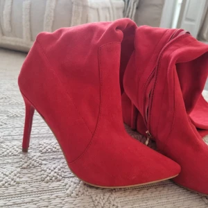 Röda stövletter från Christian Louboutin - Lårhöga röda stövletter från "Christian Louboutin' med spetsig tå och hög klack. Skorna har en dragkedja på insidan för enkel på- och avtagning. Stl 36, aldrig använda.  Kommer med kartong mm