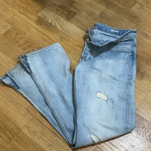 Ljusblå jeans med slitningar - Säljer ett par ljusblå jeans med coola slitningar och råa kanter. De har en klassisk femficksdesign och knappgylf. Perfekta för en avslappnad stil jag har inte använda den mycket den är helt ny absolut 