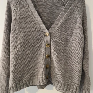 Grå stickad kofta från Rut m.fl. - Säljer en mysig grå stickad kofta från Rut m.fl. med v-ringning och knappar framtill. Perfekt för kyliga dagar och enkel att matcha med olika outfits. 🧶