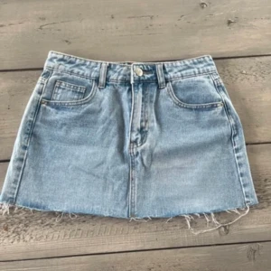 Blå jeanskjol - Trendig blå jeanskjol med rå kant. Perfekt för en avslappnad stil. Kjolen har en knapp och dragkedja framtill.