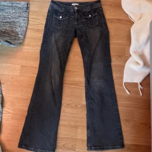 Lågmidjade bootcut jeans - Snygga svarta, lågmidjade bootcut jeans med två framfickor med lock och knappar. Jeansen har en klassisk femficksdesign och en bekväm passform. Perfekta för en avslappnad stil. Strl 158 men passar mig som har XS, ibland S!
