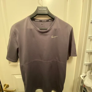 Grå Dri-FIT t-shirt från Nike - Säljer en grå Dri-FIT t-shirt från Nike, perfekt för löpning. T-shirten har en enkel design med korta ärmar och Nike-logga på bröstet. Materialet är lätt och andas bra, vilket gör den idealisk för träning.
