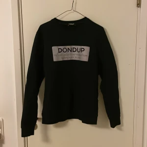 Svart tröja från Dondup - Säljer en stilren svart tröja från Dondup med tryck på framsidan. Tröjan är långärmad och tillverkad i Italien. Perfekt för en chill och grisch look. perfekt nu inför våren och till sommarkvällarna. Nypris är 190 € på glamood.com den är slutsåld där så den är sällsynt. När tröjan fotas med blixt blir trycket i reflex! Passar S