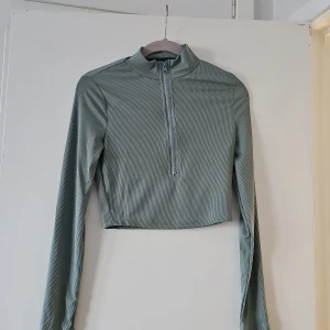 Grön ribbad croppad tröja från SHEIN - Snygg grön ribbad tröja från SHEIN med dragkedja framtill. Tröjan är croppad och har långa ärmar, perfekt för en trendig look. Passar bra till både jeans och kjol.