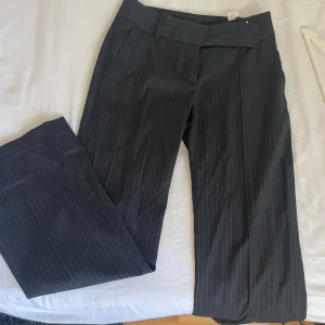 Svarta kostymbyxor - Snygga svarta kostymbyxor med diskreta ränder. Byxorna har en klassisk design med knappar och dragkedja i midjan. Perfekta för en stilren look. De är från ZARA BASIC, hör av er vid intresse så diskuterar vi ett pris🤗