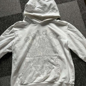 Vit spider hoodie - Säljer en vit hoodie från Spider med ett coolt spindelnätsmönster på framsidan. Tröjan har en klassisk känguruficka och en bekväm huva. Perfekt för en avslappnad stil.