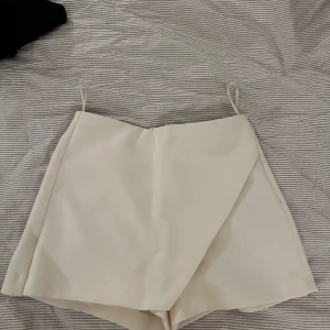 Vita omlott shorts - Snygga vita skorts med omlott-design som ger en stilren look. Perfekta för varma dagar med sin lätta och bekväma passform. De har en diskret dragkedja i sidan för enkel på- och avtagning.