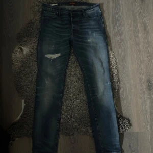 Jack & Jones jeans med slitningar - Snygga blå jeans med slitningar på låret och en modern tvättad look. De har en klassisk femficksdesign och en dragkedja. Perfekta för en avslappnad stil.