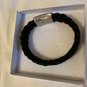 Svart flätat armband med metallspänne - Snyggt svart flätat armband med ett stilrent metallspänne. Perfekt accessoar för en modern look. 