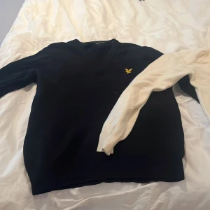 Svart tröja från Lyle & Scott - Säljer en stilren svart tröja från Lyle & Scott med v-ringning och deras ikoniska logga på bröstet. Perfekt för en klassisk look. Tröjan har långa ärmar och är gjord i ett mjukt material.