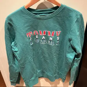 Säljer en snygg grön sweatshirt från Tommy Hilfiger med broderad logga i rött och vitt på bröstet. Tröjan har en normal passform och är perfekt för både höst och vår. Den är i mycket bra skick och superbekväm att ha på sig. Hör av dig vid intresse 