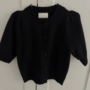 Svart kofta från Neo Noir - Snygg svart kofta från Neo Noir med trekvartsärm och knappar framtill. Perfekt för både vardag och fest. Den är i ett mjukt och bekvämt material som håller dig varm under kyliga dagar. Ett måste i garderoben!