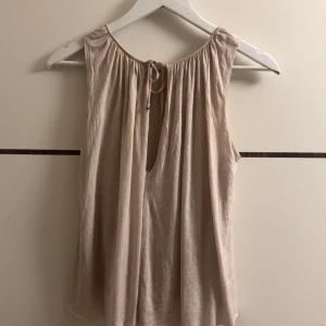 Ljusrosa ärmlös topp - Säljer en superfin ljusrosa ärmlös topp med knytning fram. Perfekt för sommardagar eller som ett lager under en kofta. Toppen har en lös passform och är gjord i ett mjukt material som känns skönt mot huden.