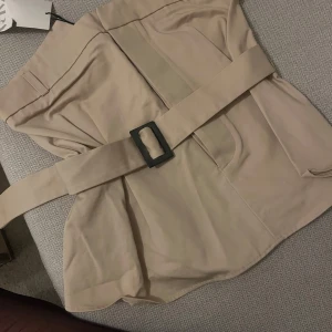 Beige topp med bälte - Säljer en stilren beige top med bälte och fyrkantigt spänne. Perfekt för att ge en elegant touch till din outfit. Aldrig använd, prislapp fins kvar. Ordinarie pris 399kr (Zara) 