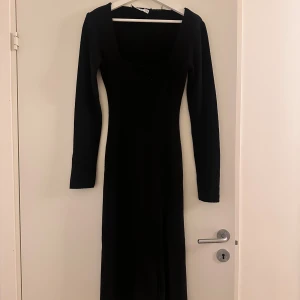 Svart långklänning med slits - Snygg svart stickadlångklänning. Den har en djup fyrkantig urringning och långa ärmar, perfekt för höst och vinter. Klänningen har några skavanker men det syns på bilderna.