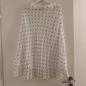 Vit prickig kjol - Säljer en superfin lång vit kjol med svarta prickar. Den har en luftig och fladdrig design. Perfekt för både vardag och festliga tillfällen. 