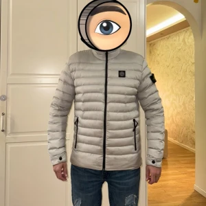 Vit pufferjacka från Stone Island - Säljer en snygg vit pufferjacka från Stone Island i mycket bra skick. Jackan har en dragkedja framtill och två praktiska fickor med dragkedjor. Den är quiltad och har en broderad logga på ärmen. Perfekt för kyliga dagar!