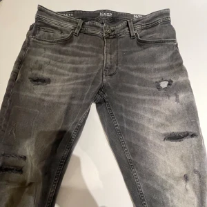 Grå jeans från Icono - Säljer ett par grå jeans från Icono i bra skick. De har en cool slitningseffekt på framsidan och är perfekta för en avslappnad stil. Jeansen har en knapp och dragkedja framtill. Perfekta för höst och vår! 