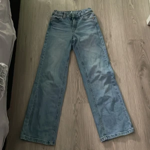 Blå jeans med hög midja - Säljer ett par snygga blå jeans med hög midja och wide fit. Perfekta för en avslappnad stil och passar till både vardag och fest. De har en klassisk femficksdesign och är i bra skick. Perfekta för höst och vår!