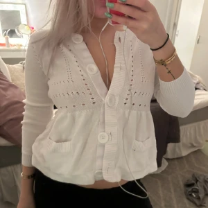 Vit kofta med stora knappar - Säljer en söt vit kofta med stora knappar och fina detaljer. Den har en lite croppad stil och är perfekt för vår och sommar. Koftan har långa ärmar och små fickor framtill. Superfin att ha över en topp eller klänning!