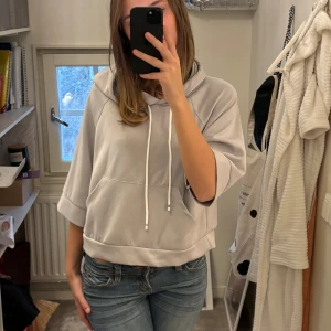 Grå hoodie med korta ärmar - Säljer en supermjuk och bekväm grå hoodie med korta ärmar och en stor ficka fram. Den har en justerbar dragsko i luvan. Stl S 
