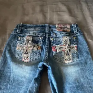 Säljer ett par snygga blå jeans från Miss Me i storlek 29. De har coola broderade korsdetaljer på bakfickorna och en klassisk femficksdesign. Jeansen är lågmidjade och har en bootcut-stil som ger en avslappnad look. lite slitna längst ner och ett par paljetter som lossnat från fickorna men paljetterna syns knappt. det lilla hålet vid innerbenet är ett litet hål som är designat att vara där, men nämner de ändå eftersom vissa gillar inte de. säljer då de är för stora för mig.💗