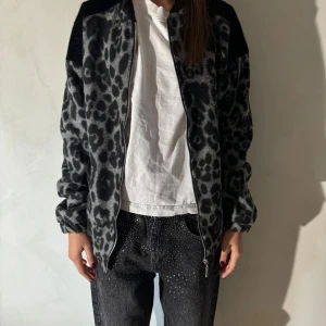 Grå leopardmönstrad jacka - Säljer en supercool grå leopardmönstrad jacka med dragkedja. Den har en loose passform och är perfekt för höst och vår. Jackan är långärmad och gjord i ett mjukt material som känns skönt mot huden. Perfekt för att ge din outfit en edgy touch!