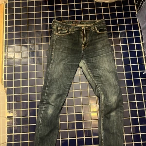 Jeans från Nudie Jeans - Säljer ett par snygga jeans från Nudie Jeans i modellen High Kai. De är i en klassisk blå färg med en slim passform och hög midja. Perfekta för både vardag och fest! 🕺