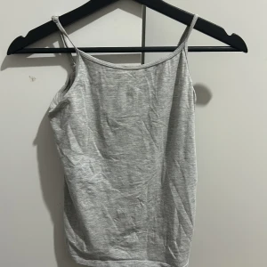 Grå ärmlös linnetopp - Säljer en enkel och stilren grå linnetopp i bomull. Perfekt för sommardagar eller som ett basplagg i garderoben. Toppen har smala axelband och en bekväm passform. Passar till både jeans och kjol!