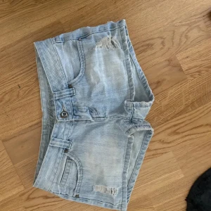 Ljusa jeansshorts med slitningar - Säljer ett par ljusa lågmidjade jeansshorts i bra skick. De har coola slitningar och en unik lappdetalj på bakfickan. Supersnygg passform! 