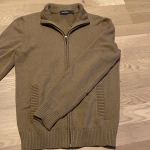 Brun stickad tröja från Dressmann - Säljer en snygg brun stickad tröja från Dressmann i storlek S. Tröjan har en dragkedja framtill och ribbade muddar vid ärmslut och nederkant. Perfekt för höst och vinter, både stilren och bekväm. Passar till både vardag och lite finare tillfällen. 🧥