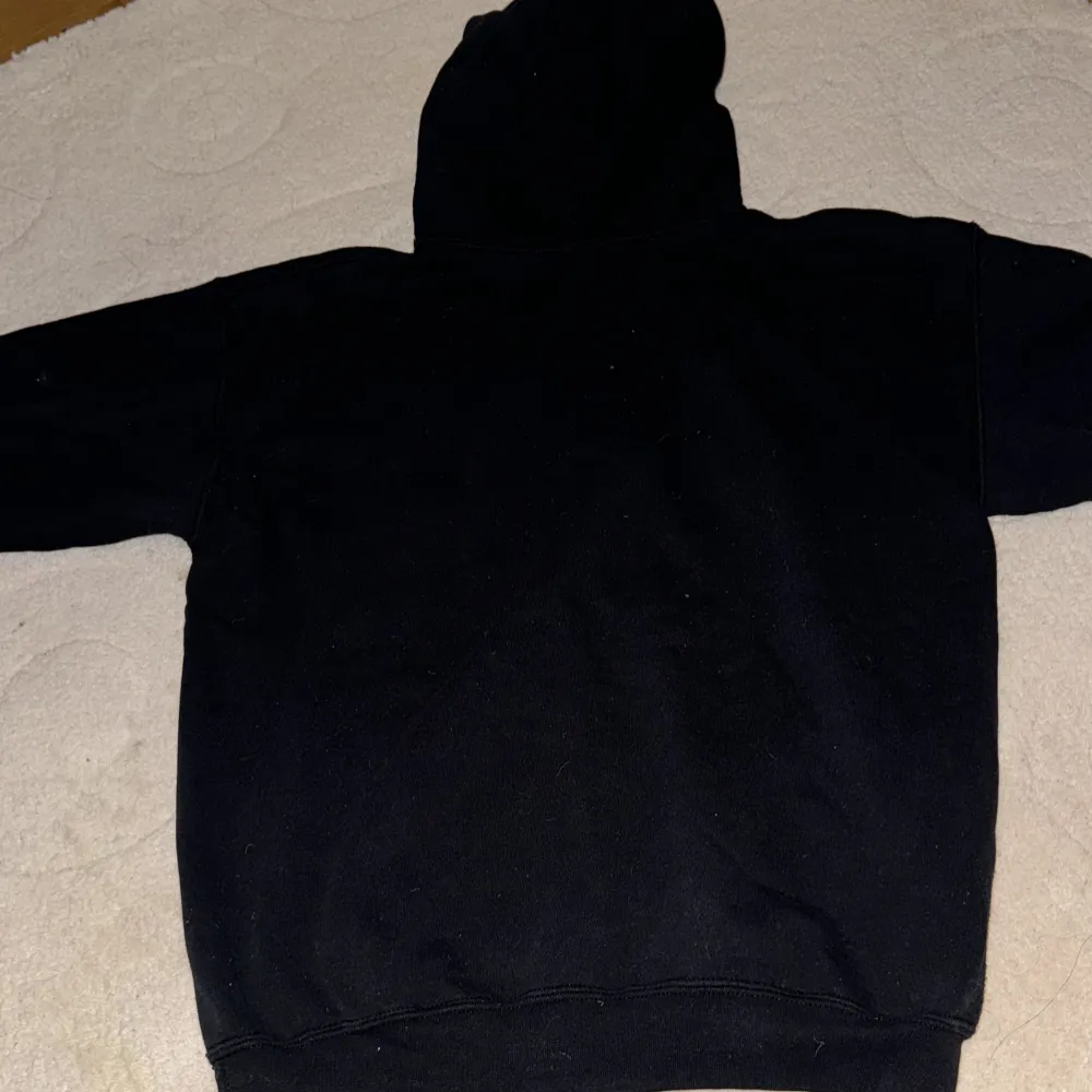 Säljer en svart hoodie från Gildan med texten 'Ekerö - Lite finare, Lite bättre' på framsidan. Den har en klassisk känguruficka och en bekväm huva. Perfekt för en avslappnad stil eller kyliga dagar. Passar både till vardags och mysiga hemmakvällar.. Hoodies.