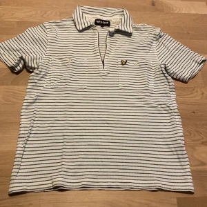 Randig pikétröja från Lyle & Scott - Säljer en snygg randig pikétröja från Lyle & Scott i storlek M. Tröjan är vit med gröna ränder och har en klassisk krage med dragkedja. Den har korta ärmar och två bröstfickor med knappar. Perfekt för en avslappnad stil!