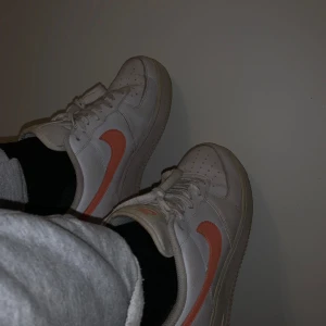 Nike Air Force 1 i vitt och orange/peach  - Säljer ett par klassiska Nike Air Force sneakers i vitt med orange/Peach swoosh. De är i bra skick enbart lite smutsiga som kan tvättas bort. Perfekta för vardagsbruk. Nypris 979kr 