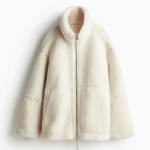 Ny cremevit teddyjacka pilejacka från H&M - Ny med tags. En tjock och varm jacka med hög krage och dragkedja framtill. Jackan är i en oversizemodell och är fodrad med ett mjukt material. Den har även två fickor framtill. Cremevit. Storlek M (oversize) HM
