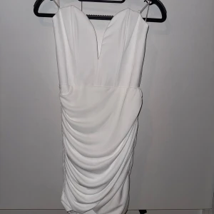 Vit klänning med drapering - Säljer en elegant vit klänning med v-ringning och draperad design. Klänningen är ärmlös och har en dragkedja bak. Perfekt för sommarens fester eller studentfiranden. Ny med taggar kvar!