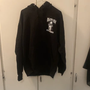 Svart hoodie från BoohooMAN med Death Row Records-tryck - Säljer en svart hoodie från BoohooMAN med coolt Death Row Records-tryck både fram och bak. Perfekt för dig som gillar streetwear och vill ha en bekväm och stilren look. Hoodien har en klassisk passform med långa ärmar och en skön huva. Perfekt för höst och vinter!