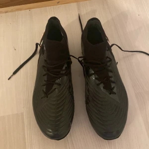 Adidas Predators Edge .1  - Säljer ett par svarta fotbollsskor från Adidas i bra skick. Säljer skorna eftersom de var småa för mig, skorna har en snygg design med vita och röda detaljer på sidan. De är perfekta för fotbollsträning och matcher. Skorna har snörning för en säker passform och är gjorda i syntetmaterial för hållbarhet. Den här använts fåtal gånger men är fortfarande som nya och går att använda mer. 