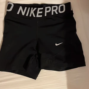 Svarta träningsshorts från Nike - Säljer ett par svarta Nike Pro träningsshorts i mycket bra skick. De är högmidjade med en elastisk midja och har en liten vit Nike-logga på benet. Perfekta för gymmet eller löprundan!