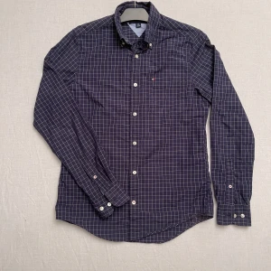 Rutig skjorta från Tommy Hilfiger - Snygg rutig skjorta från Tommy Hilfiger i mörkblått med vita rutor. Skjortan är i mycket bra skick och har långa ärmar samt knappar framtill. Perfekt för både vardag och festliga tillfällen. Riktigt grisch 🔥