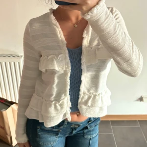 Vit kofta med volanger - Säljer en superfin vit kofta med volanger. Den är långärmad och har ett randigt mönster. Perfekt för vår och sommar, och den är i mycket bra skick. Passar perfekt till jeans❤️❤️