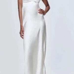 Vit långklänning från Zara - Säljer en elegant vit långklänning från Zara i storlek S. Klänningen har en slät och stilren design med smala axelband och en figurnära passform. Perfekt för sommarens fester eller en stilfull kvällslook. Materialet är mjukt och bekvämt, vilket gör den idealisk för både dag och natt.