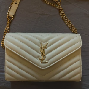 Vit quiltad axelväska från Saint Laurent - Säljer en superfin vit quiltad axelväska från Saint Laurent. Väskan har en elegant guldkedja och det ikoniska YSL-emblemet på framsidan. Perfekt för både vardag och fest! Gör din outfit 10/10. Köpt för 8000kr men säljer för 2900/3000kr 