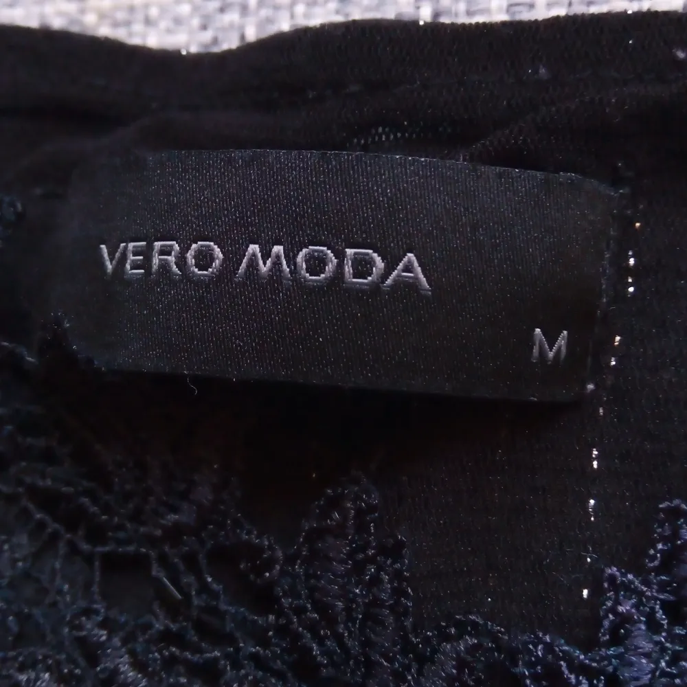 Snygg svart topp från Vero Moda i storlek M. Den har ett glittrigt mönster och spetsdetaljer på axelbanden. Perfekt för festliga tillfällen! ✨. Toppar.