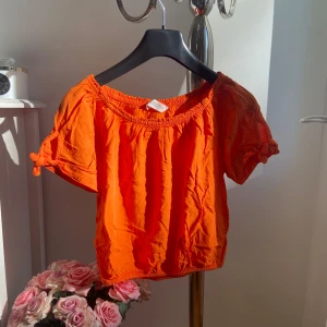 Orange kortärmad topp - Säljer en superfin orange topp med korta ärmar och elastisk halsringning. Perfekt för sommardagar! Den har en söt volangdetalj vid ärmsluten och är gjord i ett lätt och bekvämt material. Passar perfekt till både jeans och kjol. 🌞