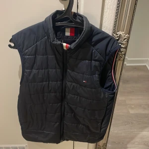 Blå Tommy hilfiger väst - Säljer en svart quiltad väst i mycket bra skick. Den har en dragkedja framtill och är perfekt för höst och vår. Västen är i storlek XS och har en stilren design med en liten logga på bröstet och passar alla upp till m. Skicka pris förslag eller byte 