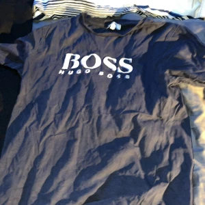 Svart t-shirt från Hugo Boss - Säljer en svart t-shirt från Hugo Boss i bra skick. Den har en klassisk design med vit logga på bröstet. Perfekt för vardagsbruk eller en avslappnad kväll ute. Passar bra till jeans eller shorts!