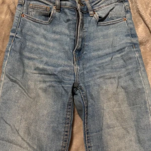 Blå jeans med slitningar - Säljer ett par snygga blå jeans med slitningar på knäna. De har en klassisk femficksdesign och en bekväm passform. 