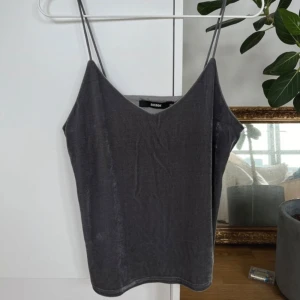 Grå sammetstopp från Bik Bok - Säljer en superfin grå sammetstopp från Bik Bok i storlek XS. Toppen har tunna axelband och en mjuk, glansig yta som ger en lyxig känsla. Perfekt för en utekväll eller fest! 💃